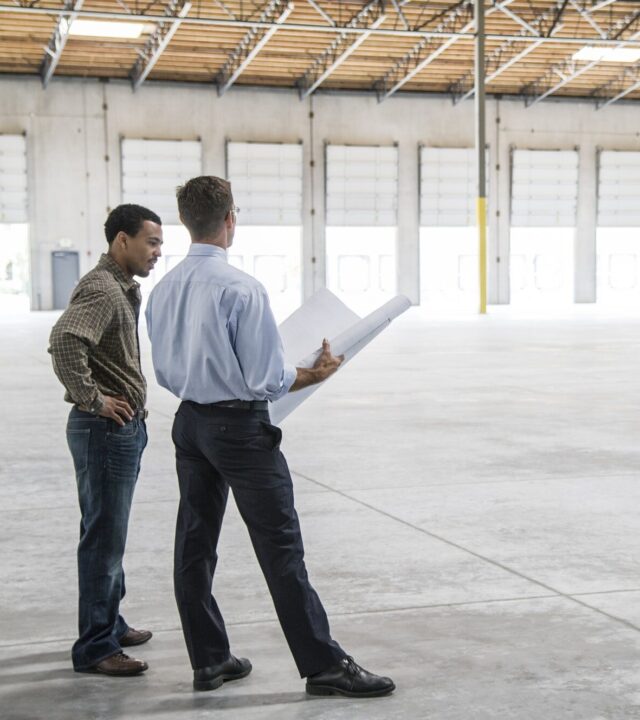 Back man owner of new warehouse and caucasian man architect going over blue print plans of new